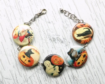 Pode incluir: Um bracelete temático de Halloween com cinco botões redondos que apresentam imagens vintage de abóboras, gatos, corujas e um fantasma. Os botões são conectados por uma corrente prateada.