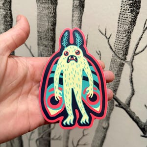 Può includere: Un adesivo di un mostro dei cartoni animati con un corpo giallo, ali blu e occhi rossi. Il mostro ha un corpo peloso e sta in piedi con le ali spiegate.