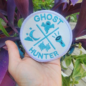 May include: White round patch with blue embroidery. The patch says "Ghost Hunter" with a ghost, crescent moon, cloud, and flashlight.