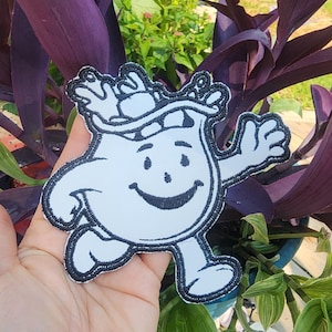 May include: White embroidered iron-on patch of a cartoon character with a smiling face and a straw hat. The character is running and has a white body with black outlines.