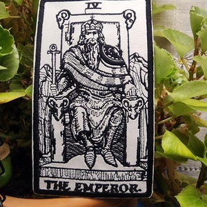 May include: A rectangular, black and white tarot card featuring an illustration of The Emperor. The card shows a seated figure with a long beard, crown, and scepter. The card is bordered in black with the Roman numeral IV at the top and the words "THE EMPEROR" at the bottom.