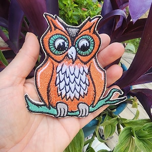 May include: Orange and green embroidered owl patch with white accents. The owl is perched on a green branch.