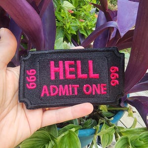 May include: Black fabric patch with white stitching. The patch is shaped like a ticket and says "HELL ADMIT ONE" in red letters with the number "666" on either side.