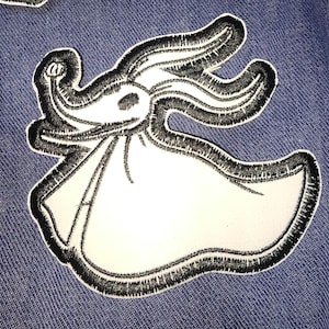 May include: Black and white embroidered iron-on patch of a ghost-like character with a long, thin body and a large, round head. The character has a large, round nose and a small mouth. The patch is on a blue denim background.