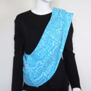 May include: A light blue baby carrier with a white bone pattern. The carrier is being worn by a person wearing a black shirt.