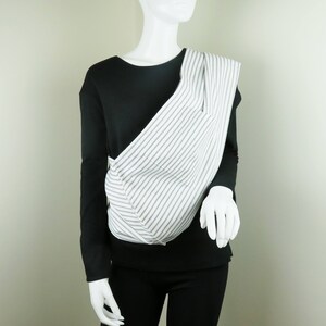 May include: A white and gray striped baby carrier with a black long-sleeved shirt underneath.