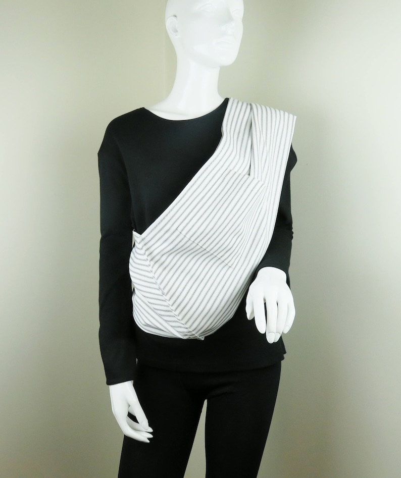 May include: A white and gray striped baby carrier with a black long-sleeved shirt underneath.