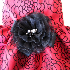 May include: A red satin dress with a black floral pattern and a large black flower embellishment with silver beads.