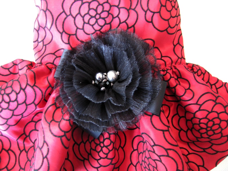 May include: A red satin dress with a black floral pattern and a large black flower embellishment with silver beads.