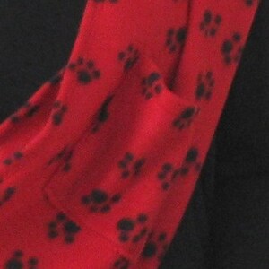 May include: Red fleece scarf with a black paw print pattern. The scarf has a pocket on the side.