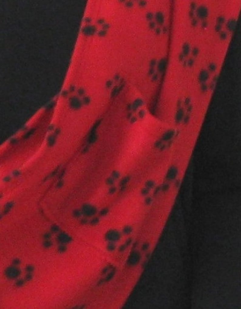 May include: Red fleece scarf with a black paw print pattern. The scarf has a pocket on the side.