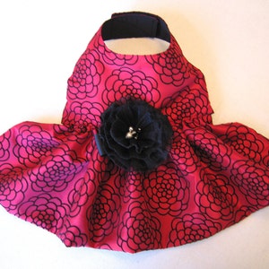May include: A pink dog dress with a black floral pattern and a large black flower accent.