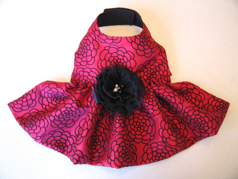 May include: A pink dog dress with a black floral pattern and a large black flower accent.