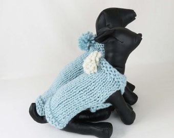 May include: Two blue knitted dog sweaters with white pom-poms on the hoods. The sweaters are on black mannequin dogs.