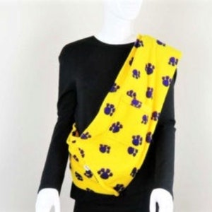 May include: Yellow fabric carrier with purple paw prints. The carrier is worn over one shoulder and is made of a soft, comfortable fabric.