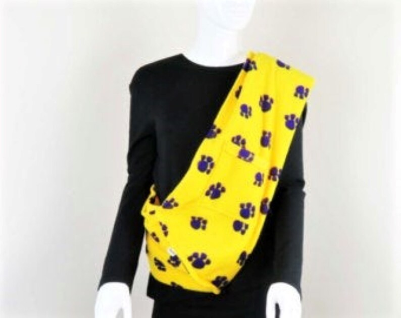 May include: Yellow fabric carrier with purple paw prints. The carrier is worn over one shoulder and is made of a soft, comfortable fabric.