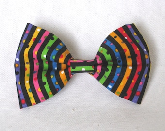 May include: A colorful bow tie with a striped pattern in black, orange, yellow, green, pink, and blue. The bow tie also features small, colorful polka dots. The accessory is likely made of fabric and is suitable for various occasions.