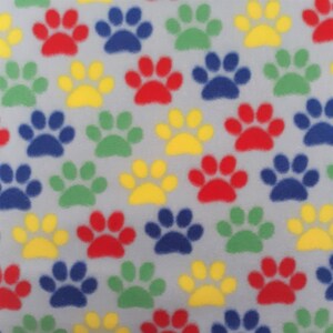 May include: A grey fabric with a repeating pattern of colourful paw prints. The paw prints are in red, blue, green, and yellow.