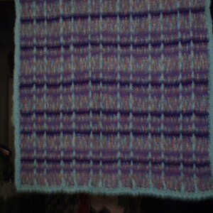 May include: A blue and purple knitted blanket with a textured pattern. The blanket has a light blue border.