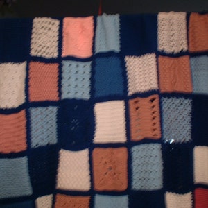 May include: A crocheted blanket with a patchwork design. The blanket is made up of squares in various shades of blue, pink, and white.
