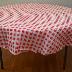 May include: Red and white checkered tablecloth on a round table with black metal legs.