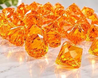 May include: A collection of numerous faceted orange acrylic gems shaped like diamonds. Each piece features a translucent, vibrant orange color with multiple angular surfaces that catch the light, creating a sparkling effect across the group.