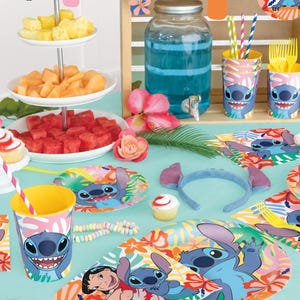 Puede incluir: Una escena festiva de fiesta con tem&aacute;tica tropical. La mesa est&aacute; decorada con art&iacute;culos de fiesta con el tema de Stitch, que incluyen vasos, platos y una diadema. Frutas frescas, cupcakes y un dispensador de bebidas grande se suman al ambiente festivo. Decoraciones coloridas y acentos florales completan el look.