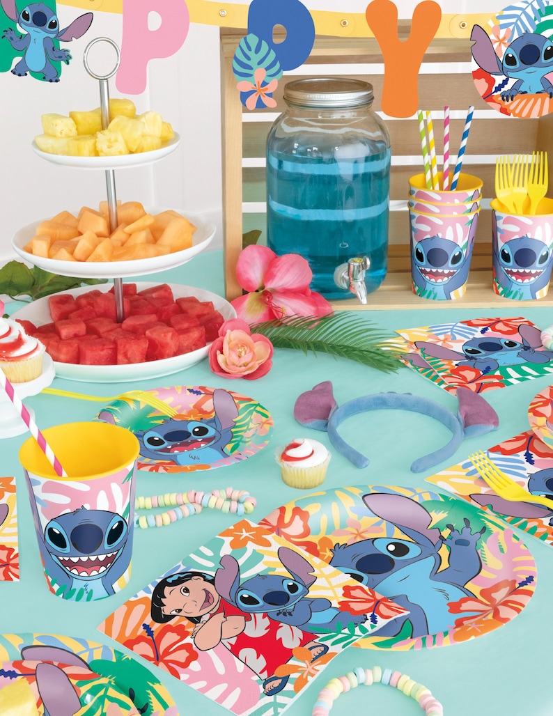 Puede incluir: Una escena festiva de fiesta con tem&aacute;tica tropical. La mesa est&aacute; decorada con art&iacute;culos de fiesta con el tema de Stitch, que incluyen vasos, platos y una diadema. Frutas frescas, cupcakes y un dispensador de bebidas grande se suman al ambiente festivo. Decoraciones coloridas y acentos florales completan el look.