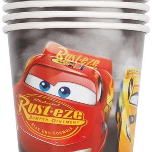 May include: Stack of paper cups featuring Lightning McQueen from the Cars movie. The cups are red with white rims and the Rust-eze logo. The background is a blurred image of a race track.