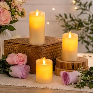 May include: Three cylindrical LED pillar candles with a warm, glowing flame effect. The candles are cream-colored with a smooth wax-like finish and uneven, melted-style tops. They emit a soft, golden light, creating a gentle illumination.