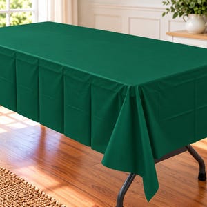 May include: A rectangular dark green tablecloth with a pleated skirt design draped over a folding table. The fabric features a smooth, solid-colored surface that extends over the top and hangs down the sides with structured vertical folds.
