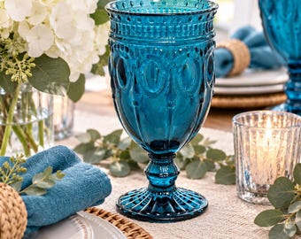 May include: A deep blue glass goblet featuring a textured, embossed pattern with vertical fluting and a scalloped base. The vessel has a wide rim, a tapered stem, and a circular foot, crafted from translucent blue glass with a polished finish.