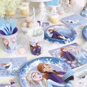 Puede incluir: Una mesa de fiesta con tem&aacute;tica de Frozen. Incluye platos, vasos, servilletas y cubiertos en tonos azules y blancos, adornados con im&aacute;genes de Elsa, Anna y Olaf. La escena est&aacute; decorada con cupcakes, tarta y otras golosinas.