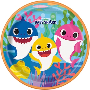May include: Round paper plate featuring the Baby Shark family: a blue shark, a pink shark, and a yellow shark. The plate has an orange border and a blue background with seaweed and coral.