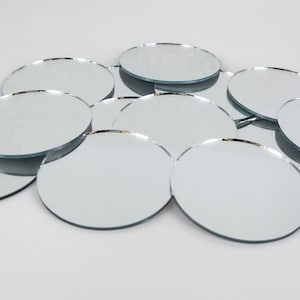 May include: A pile of round, silver-backed mirrors with a beveled edge. The mirrors are various sizes and are arranged in a random pattern.