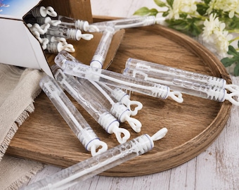 May include: A collection of clear plastic bubble wands with white heart-shaped handles. The wands are cylindrical, filled with bubble solution, and feature a white wand applicator inside. Several wands are scattered, while others remain in a box.