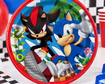 May include: A round paper plate with a red rim featuring a graphic illustration of the characters Sonic the Hedgehog and Shadow the Hedgehog. The background shows a blue sky, green palm trees, and a checkered ground pattern with a yellow flower.