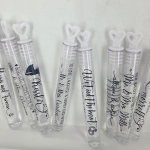 May include: Clear plastic bubble wands with white heart-shaped handles. The wands are decorated with black text, including phrases like "Always and Forever" and names like "Kessler". Ideal for weddings or celebrations.