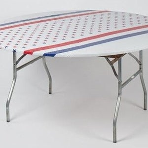 May include: A white round tablecloth with a red, white, and blue star and stripe pattern. The tablecloth is on a round folding table with silver legs.