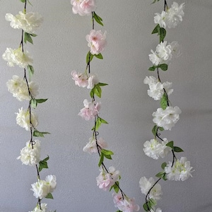 May include: Two strands of artificial flower garland with white and pink blossoms. The garland is made of plastic and wire and is suitable for decorating a home or party.