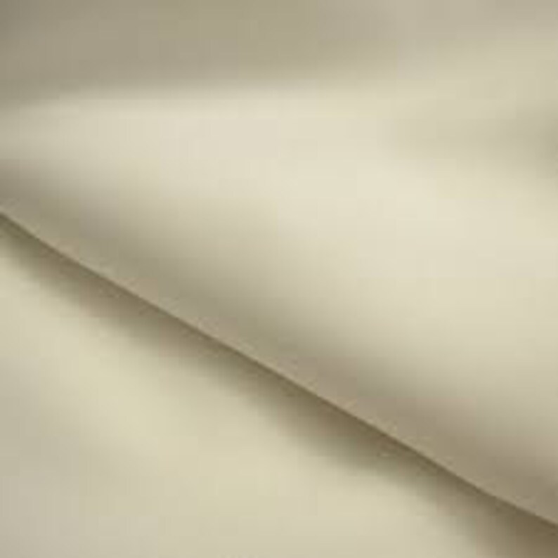 May include: A close-up shot of a folded, off-white fabric. The material appears smooth and drapes softly, with subtle shadows and highlights suggesting its texture and form. The fabric's neutral color and gentle folds create a sense of elegance and simplicity.