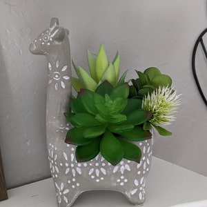 May include: A gray ceramic giraffe planter with white polka dots, featuring a variety of green succulents.