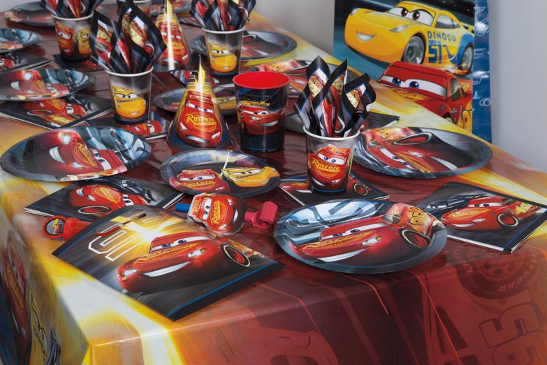 May include: A party table setting featuring Lightning McQueen from the Cars movie. Includes plates, cups, napkins, and party hats. The color scheme is red, yellow, and black, with images of the race car. Perfect for a child's birthday party.
