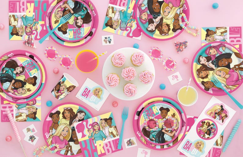 May include: Pink and yellow Barbie themed party supplies, including plates, napkins, cups, and cupcake wrappers. The plates feature a group of diverse Barbie dolls with the text "Barbie" and "Girls" on them. The napkins have a pink and yellow design with the text "Barbie" on them. The cups are pink and have a white rim. The cupcake wrappers are pink and have a white rim. The cupcakes are pink and have white frosting.