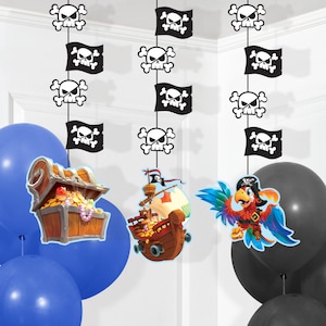 May include: Three pirate-themed hanging decorations with black and white skull and crossbones flags, a treasure chest, a pirate ship, and a parrot. The decorations are hanging from blue and black balloons.