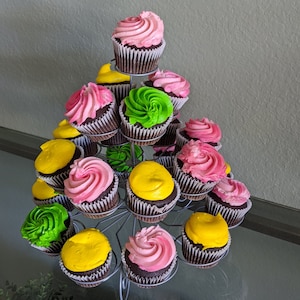 May include: A tiered cupcake stand displays chocolate cupcakes with colorful frosting. The frosting colors include pink, green, and yellow. The cupcakes are arranged on a silver metal stand, creating a visually appealing dessert display.