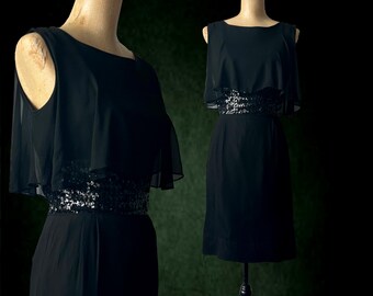 Può includere: Due abiti neri su manichini. Gli abiti hanno un design simile, con una cintura di paillettes e un top fluido e a strati. Gli abiti sono lunghi fino al ginocchio e sembrano essere realizzati in un tessuto leggero, adatti per occasioni formali.