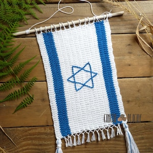 May include: A white crocheted wall hanging with blue stripes and a blue Star of David in the center. The hanging has white tassels on the bottom and is attached to a wooden dowel.