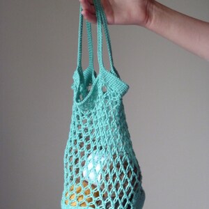 May include: A turquoise crocheted mesh bag with a single handle. The bag is filled with yarn balls.