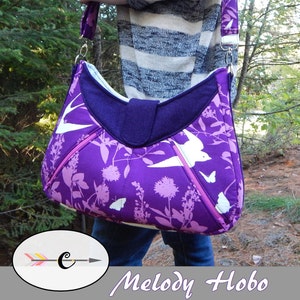 May include: A purple and white floral print hobo bag with a white strap and a silver clasp. The bag is semi-structured and has a zipper closure. The bag is being worn by a person in a striped sweater and jeans. The text "Melody Hobo" is displayed below the image. The text "The stylish, semi-structured hobo bag for the everyday." is displayed below the text "Melody Hobo".